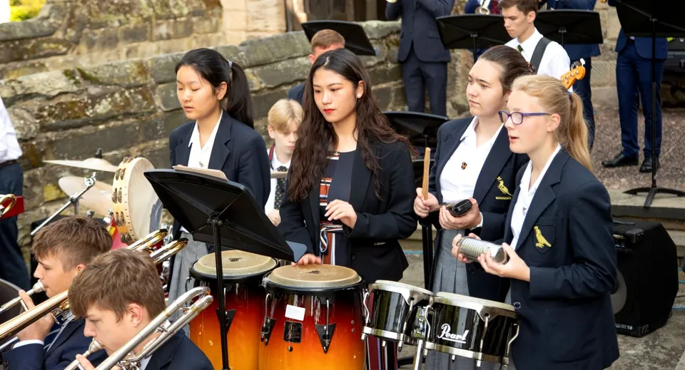Studenti della Repton School suonano vari strumenti a percussione davanti a un edificio in pietra.