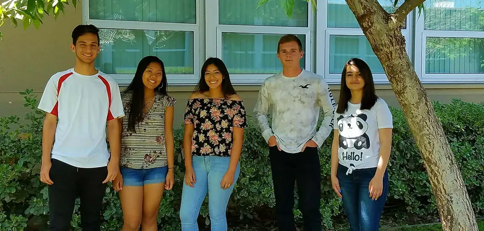 Un gruppo di cinque studentesse e studenti in piedi davanti a un edificio verde nel campus della El Cajon Valley High School.