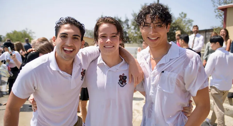 Tre studenti della JSerra Catholic High School sorridono all'aperto davanti ad alberi e ad altre persone.