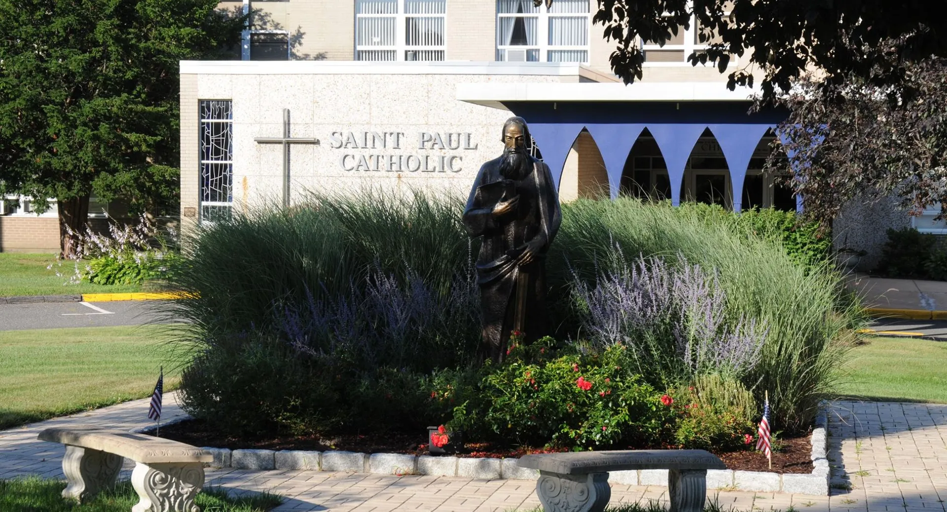Una statua di una figura religiosa si trova nel giardino ben curato sul campus della St. Paul Catholic High School con la chiesa cattolica sullo sfondo.