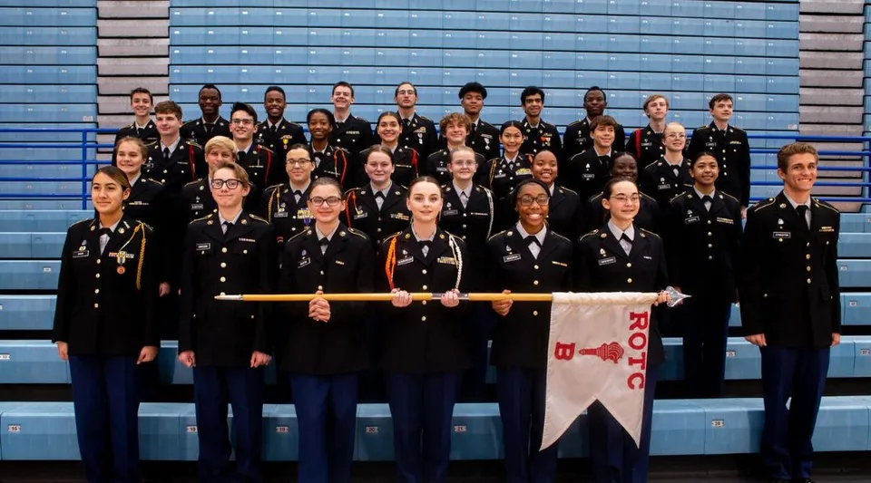 Un gruppo di studenti del Sierra Vista Unified School District in uniformi nere davanti a uno sfondo blu-grigio, che tiene in mano uno striscione.