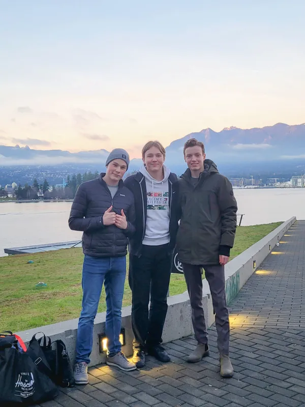 Tres chicos posando en el paseo marítimo al amanecer con montañas nevadas al fondo