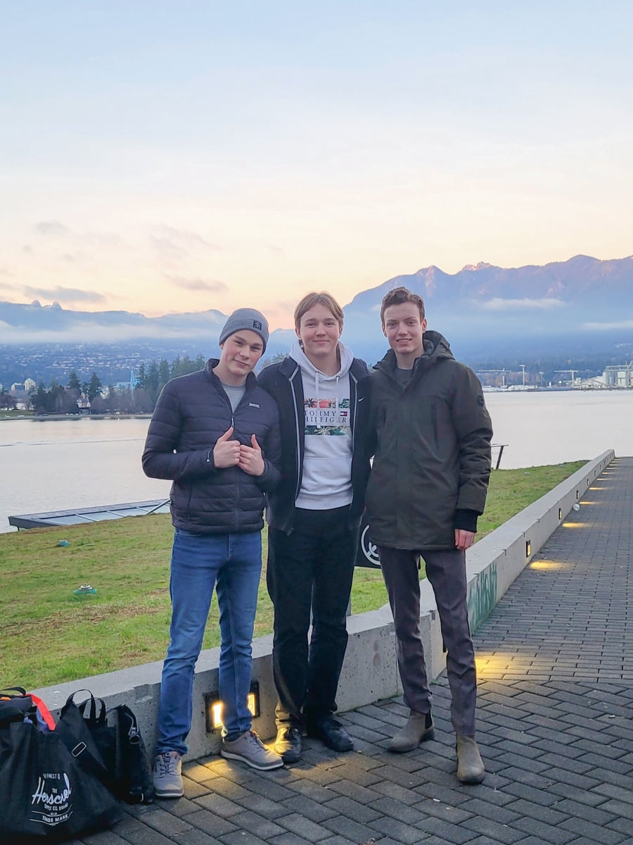 Tres chicos posando en el paseo marítimo al amanecer con montañas nevadas al fondo