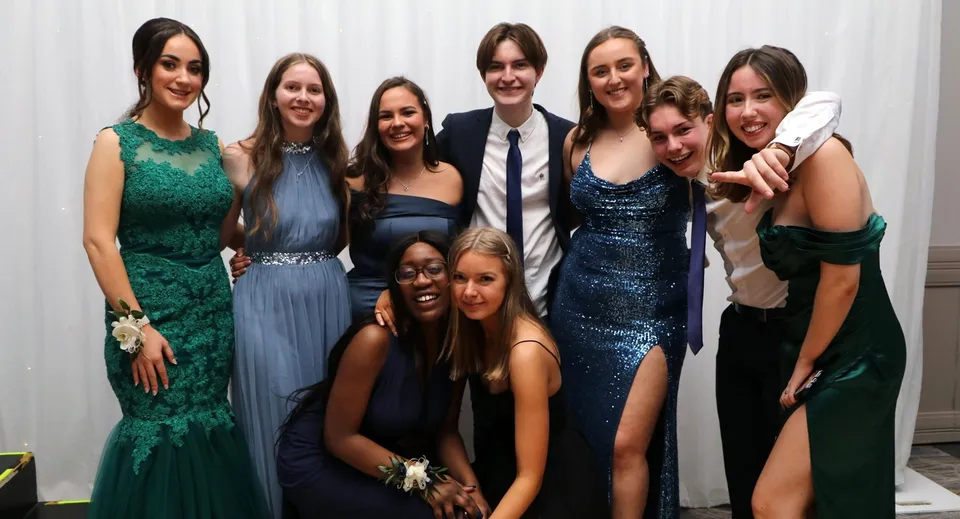 Un gruppo di persone vestite elegantemente posa insieme davanti a uno sfondo bianco nel campus del Tyndall College.