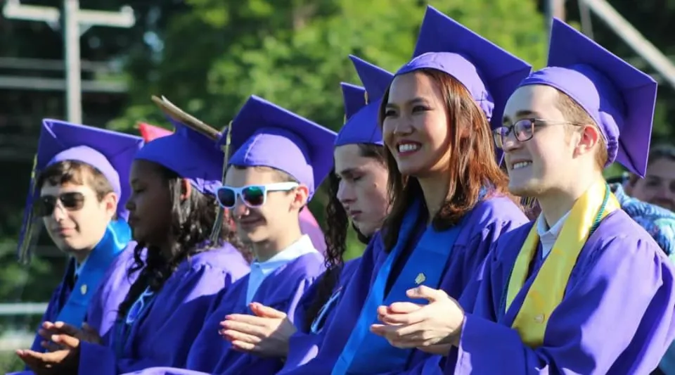 Un gruppo di diplomati in toga viola festeggia il diploma nel campus della Sparhawk School.