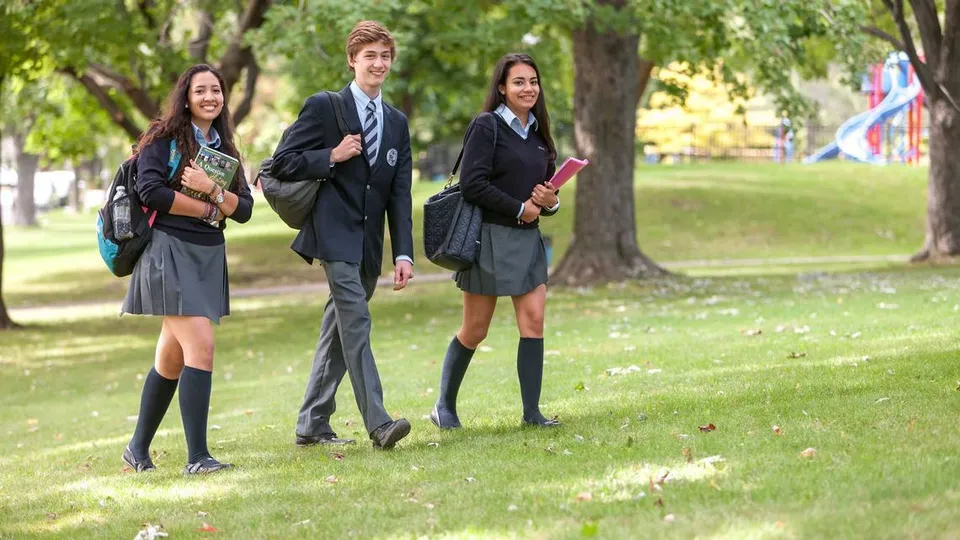 Tre studenti della Kells Academy camminano su un sentiero erboso circondato da alberi.