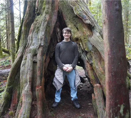 Stefan steht im hohlen Stamm eines großen Baumes in einem Wald in Kanada