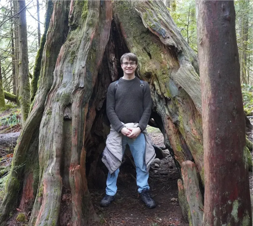 Stefan steht im hohlen Stamm eines großen Baumes in einem Wald in Kanada
