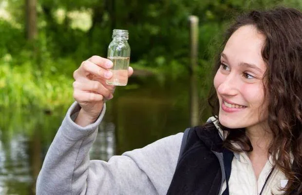 Una alumna de la Elite Preparatory Academy sostiene una pequeña botella de vidrio ante un follaje verde.