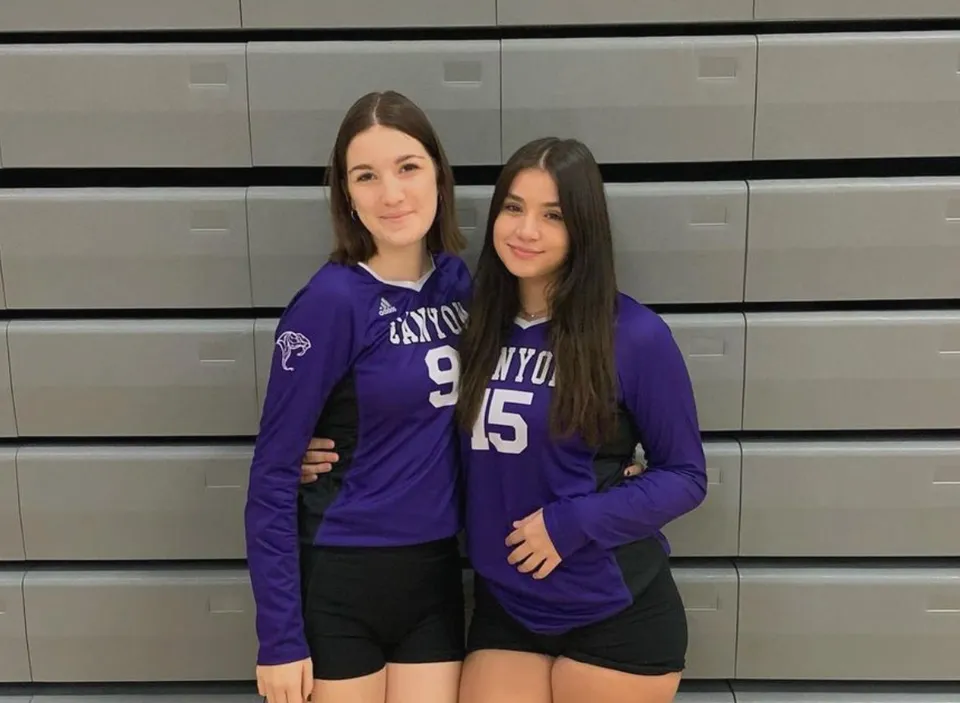Due studentesse della North Canyon High School sono in piedi davanti a uno sfondo grigio con maglie viola con i numeri 15 e 9.