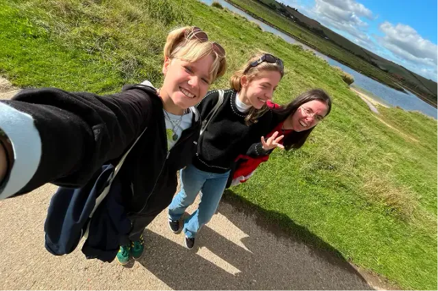 Tre amiche sorridenti si scattano un selfie su un sentiero vicino a un lago