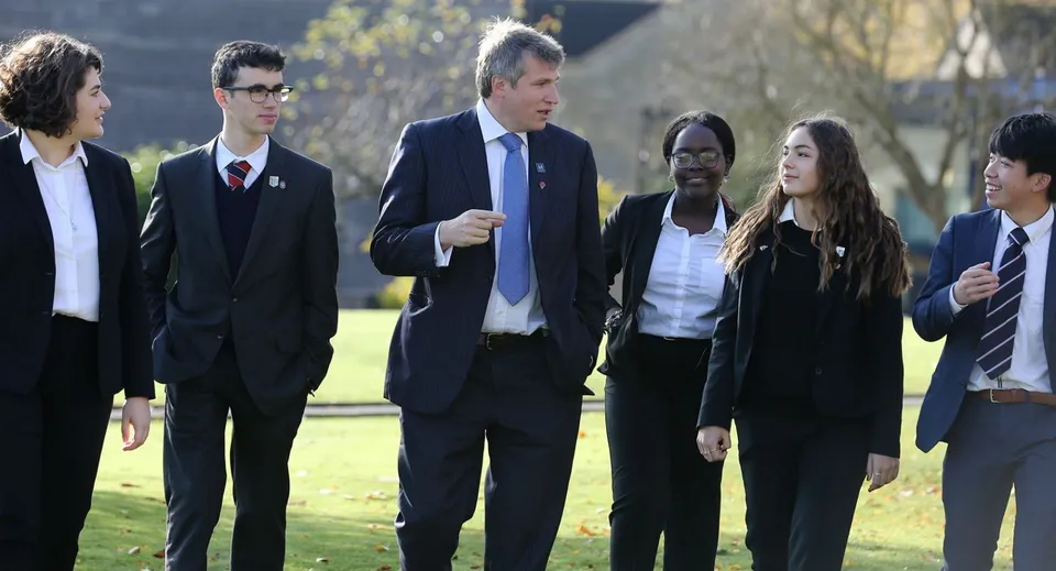Un gruppo di studenti della Monkton Combe School passeggia insieme su un prato con alberi sullo sfondo.