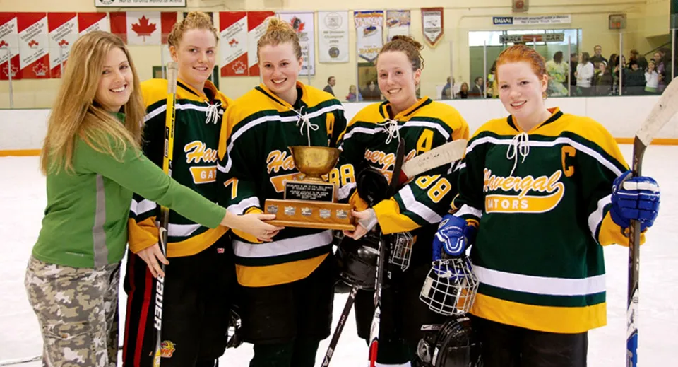 Studentesse dell'Havergal College tengono un trofeo in una pista da hockey con bandiere canadesi.