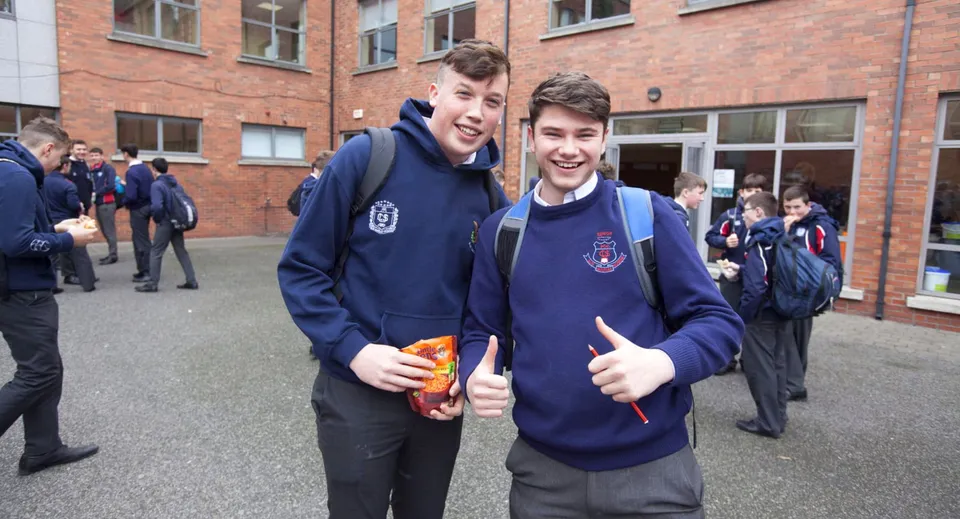 Due studenti in uniforme scolastica stanno insieme e sorridono davanti a un edificio in mattoni sul campus della Catholic University School.