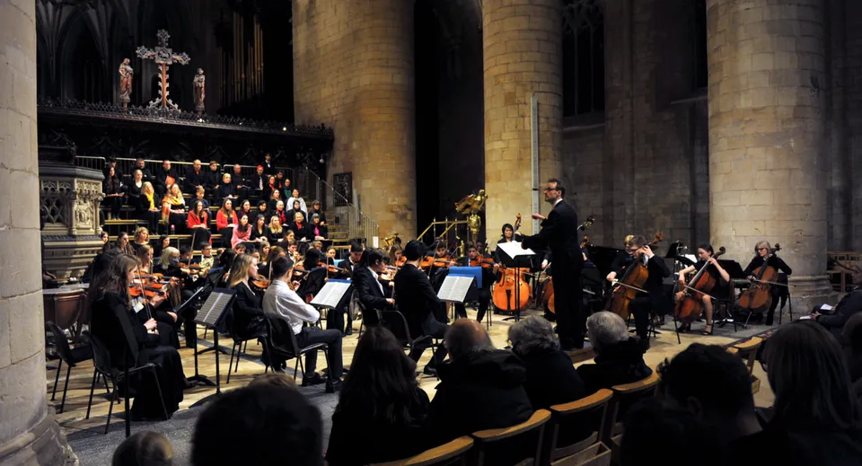 L'orchestra del Cheltenham College suona su un palco in una grande cattedrale davanti a un pubblico.