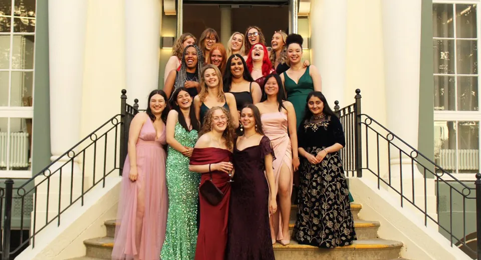 Studentesse della Brighton Girls posano insieme su una scala in abiti eleganti davanti a uno sfondo decorativo.