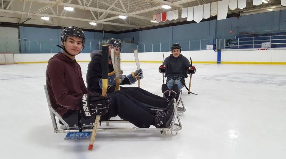 Tre studenti della Warburg School in attrezzatura da hockey su ghiaccio siedono su una panchina nel palazzetto del ghiaccio.