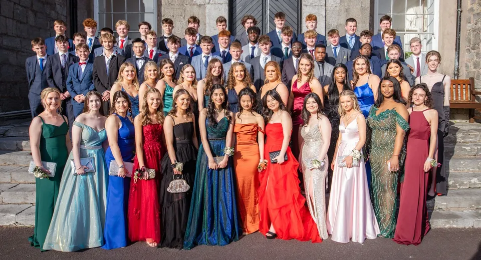 Un gruppo di studenti del Midleton College posa in abiti formali davanti a un edificio in pietra.