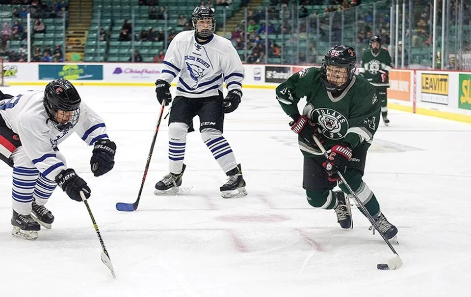 Due giocatori di hockey su ghiaccio con le maglie della squadra lottano sul ghiaccio davanti agli spettatori presso la Prince George Secondary School.