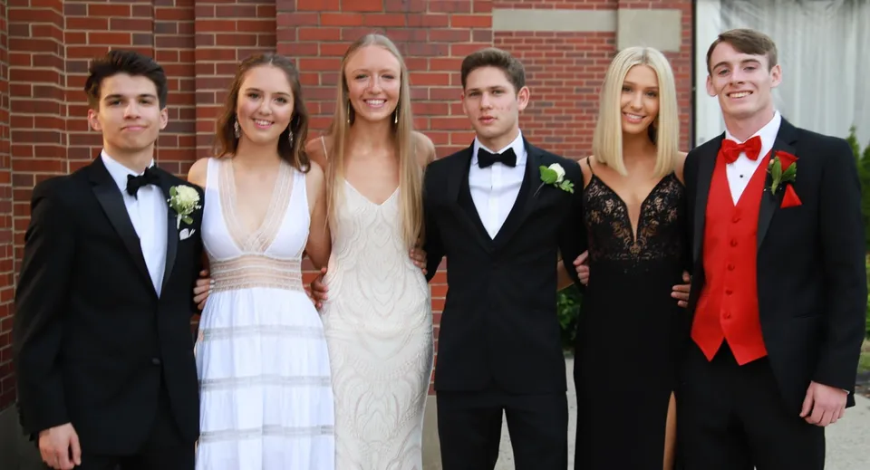 Un gruppo di persone in abito formale posa davanti a una parete in mattoni nel campus della Sugarloaf Senior High.
