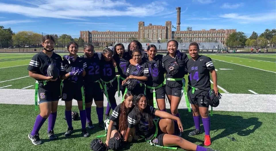 Un gruppo di studenti in divisa sportiva posa sul campo sportivo davanti all'edificio storico della Carl Schurz High School.