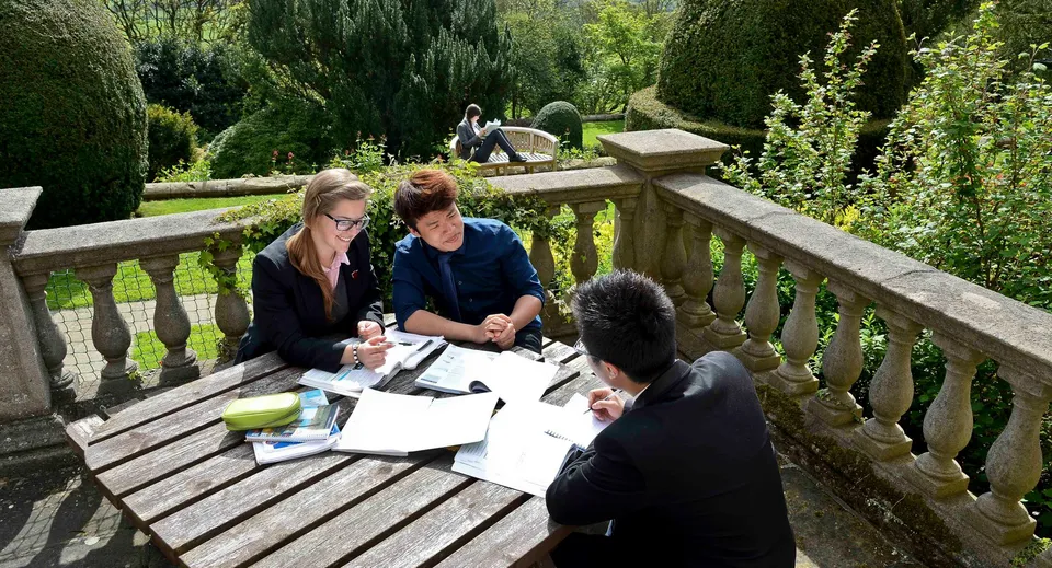 Un gruppo di studenti della Fyling Hall School si incontra attorno a un tavolo su una terrazza in legno in un giardino.