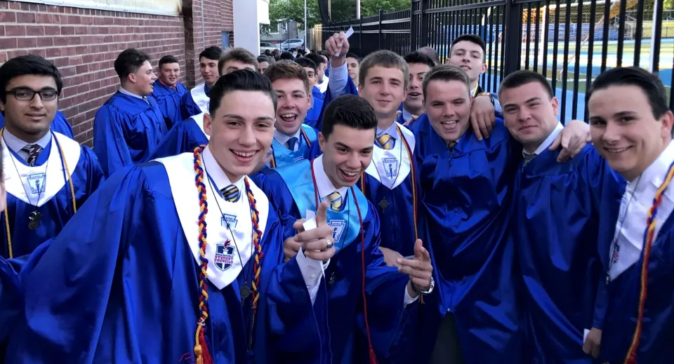 Un gruppo di studenti della St. Peter High School in toga blu da diploma posa per una foto davanti a un edificio in mattoni.