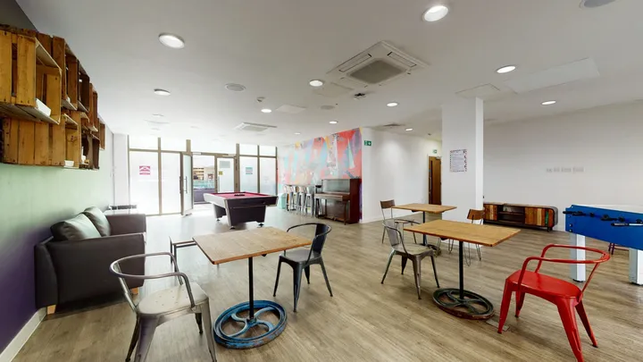 Sala común de la residencia con mesas, sillas, sofá y mesa de billar