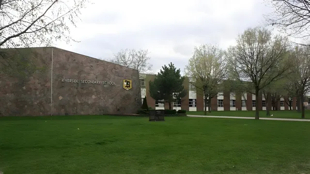 Ein grasbewachsener Hof vor einem Backsteingebäude mit Rundbogenfenstern auf dem Gelände der Riverside Secondary School.