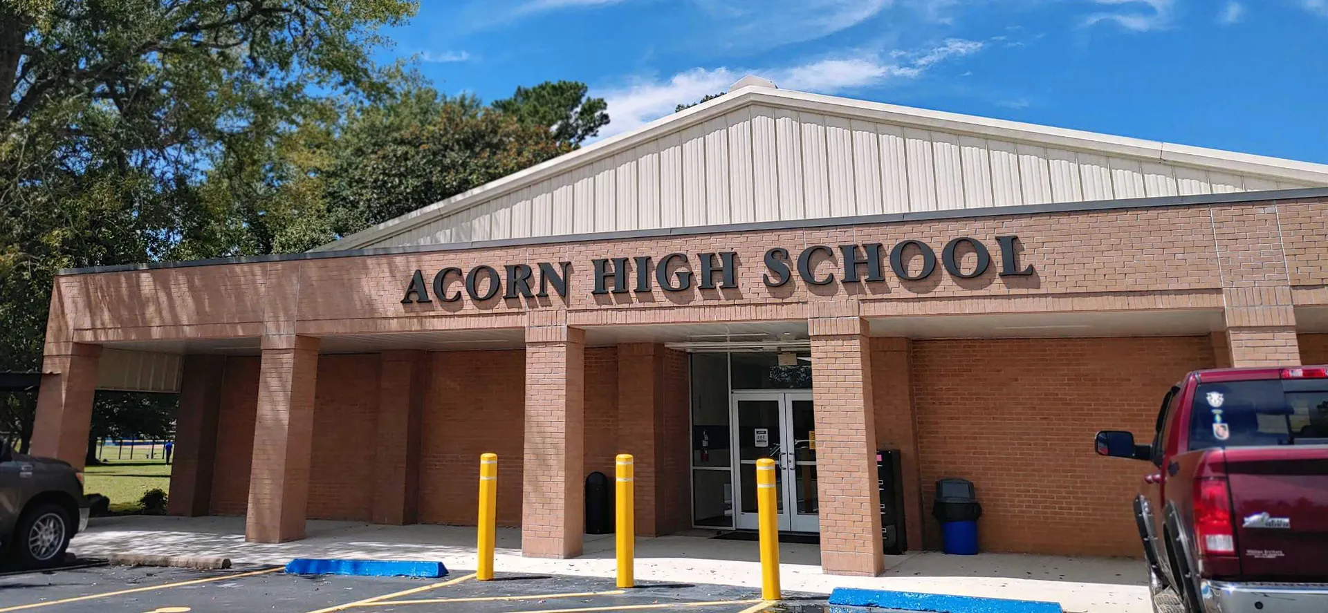 L'edificio della Acorn High School è in mattoni e legno e si erge davanti a un cielo blu limpido con alberi.