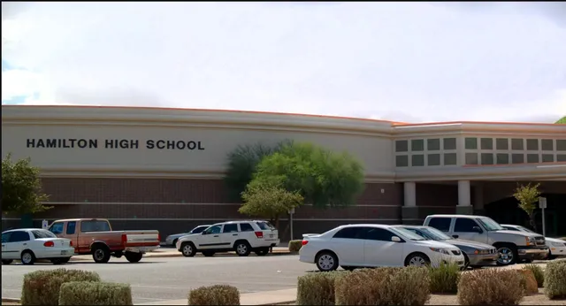 Das große Backsteingebäude der Hamilton High School mit dem Schriftzug am Gebäude und einem Parkplatz im Vordergrund.