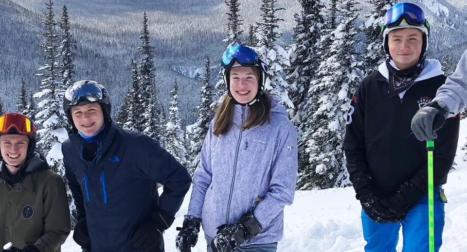 Un gruppo di studenti della Point Grey Secondary School si trova in un paesaggio forestale invernale con montagne sullo sfondo.