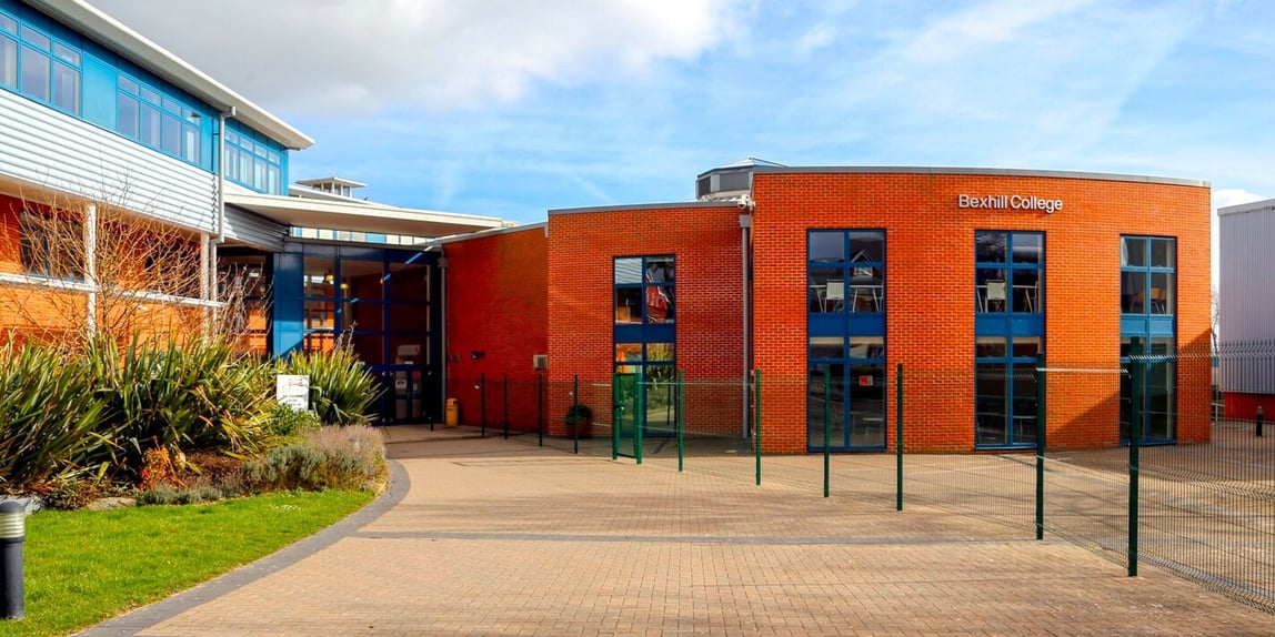 Roter Backsteinbau des Bexhill College mit Schriftzug, Glasfassade und gepflastertem Vorplatz