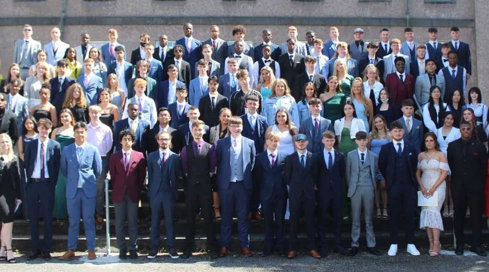 Un gruppo di persone in abito formale si trova all'aperto davanti a un edificio nel campus della Colaiste Muire Mathair.