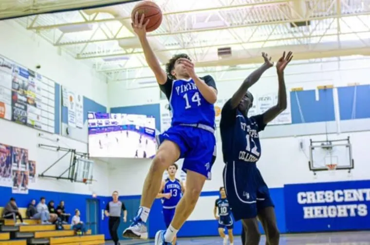 Jugador de baloncesto con uniforme azul salta a la canasta ante un defensor