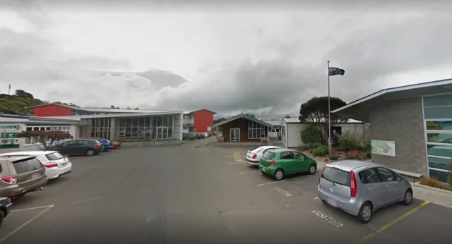 Una piccola strada di città con edifici rossi e auto parcheggiate sotto un cielo nuvoloso vicino al Newlands College.
