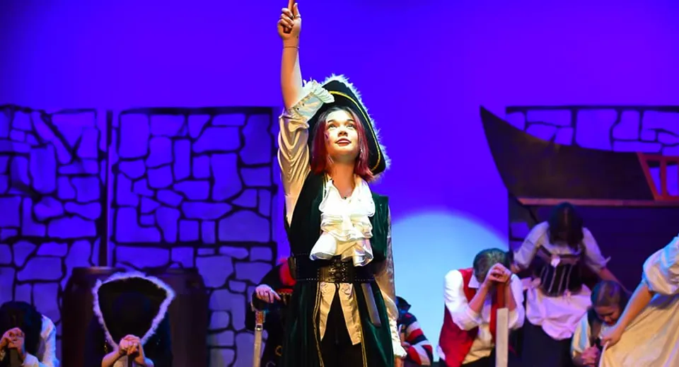 Una donna in costume è sul palco con le braccia alzate durante una rappresentazione della Salisbury High School.