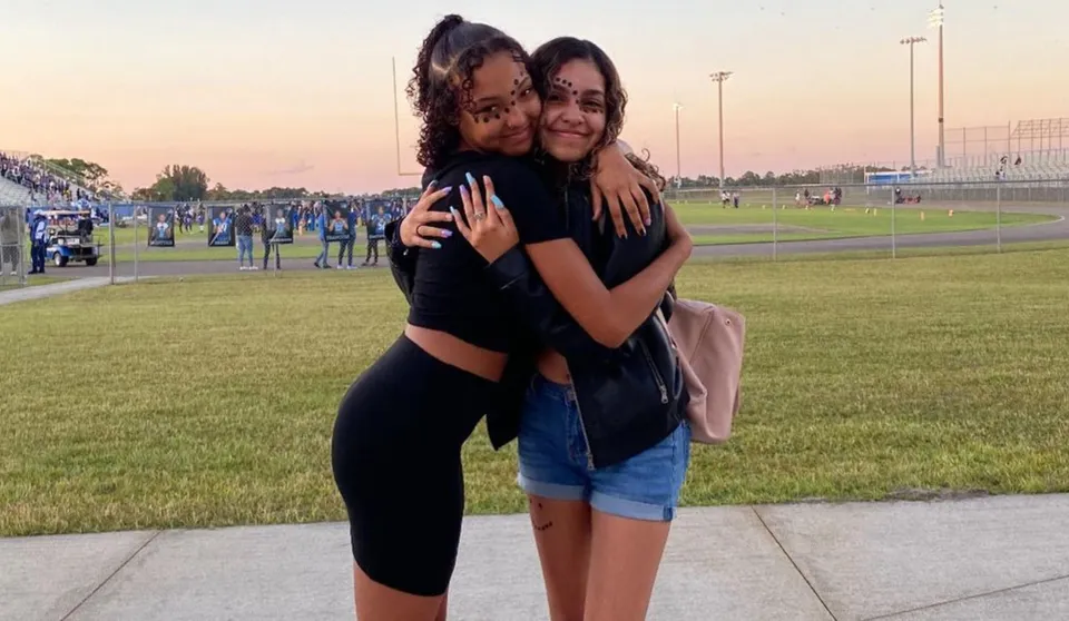 Due studentesse si abbracciano su un prato davanti allo stadio sportivo della Heritage High School.