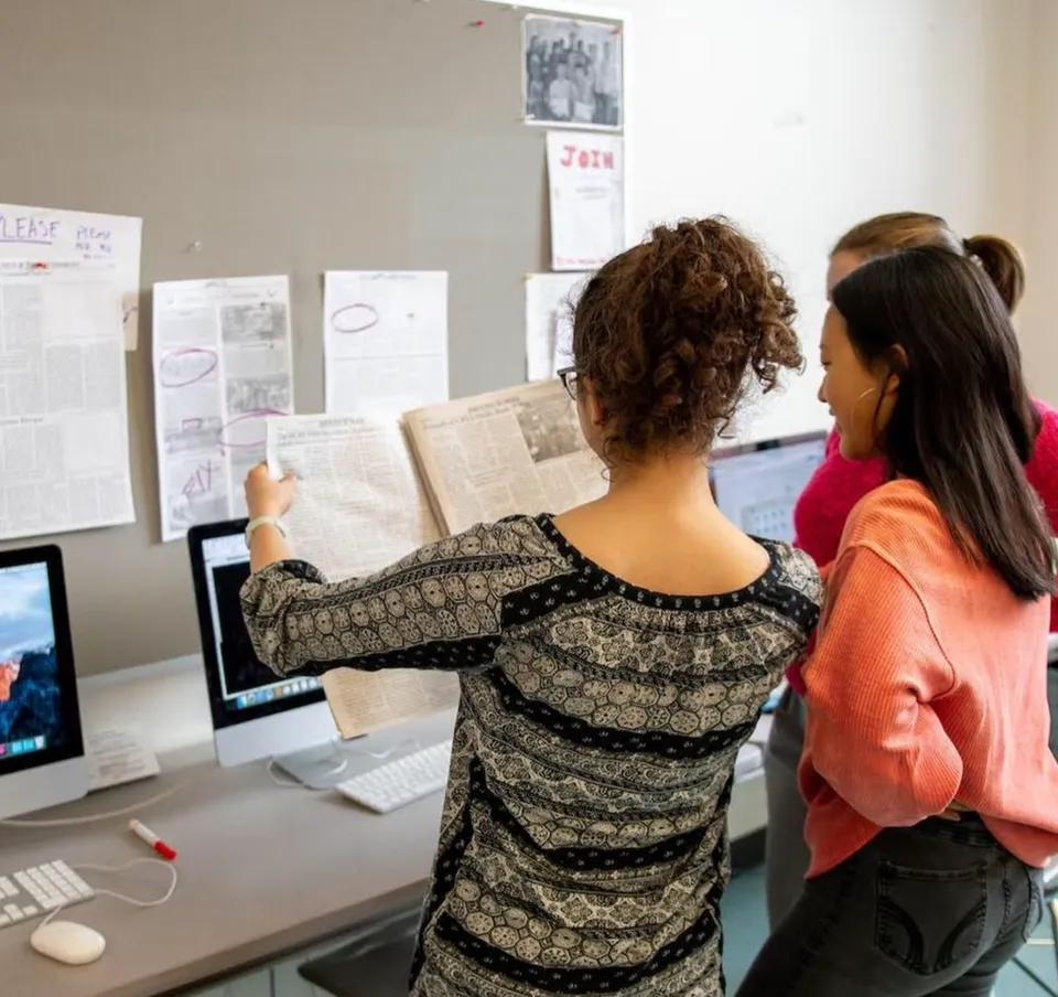 Due studentesse della Cambridge Rindge and Latin High School sono davanti a una lavagna bianca e discutono insieme dei documenti.