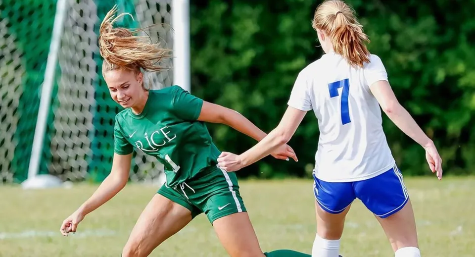 Due studentesse della Rice Memorial High School giocano a calcio su un campo con una porta visibile sullo sfondo.