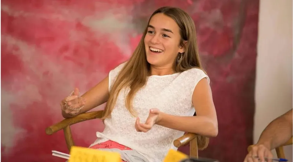 Una giovane donna sorridente sta davanti a uno sfondo rosa nel campus del Greene's College Oxford.