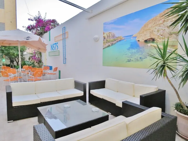 Terraza cubierta del alojamiento con sofás, mesa baja y un mural de una cala