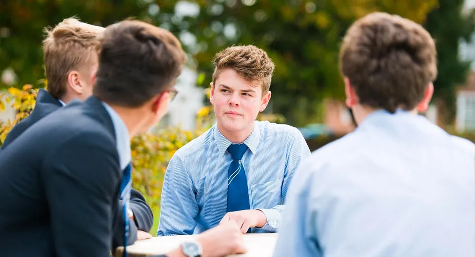 Un gruppo di studenti della Ashford School chiacchiera davanti a uno sfondo verde e fiorito.