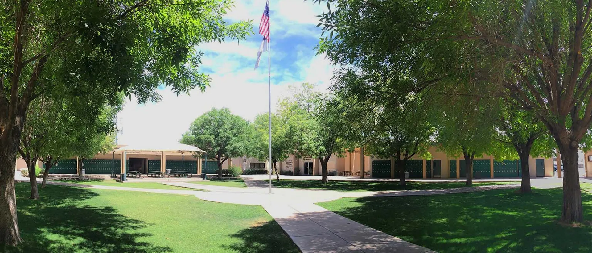 Il verde campus della Phoenix Christian Preparatory School con un sentiero verso un edificio e una bandiera americana.