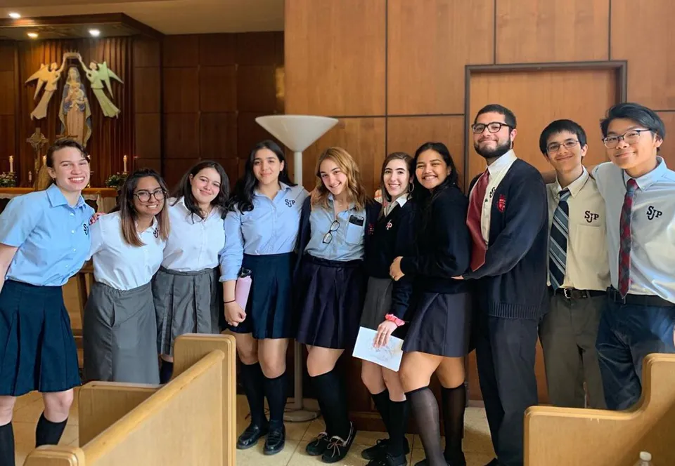 Un gruppo di studenti e studentesse posa insieme in una stanza con pannelli in legno alla Saint Johns High School.