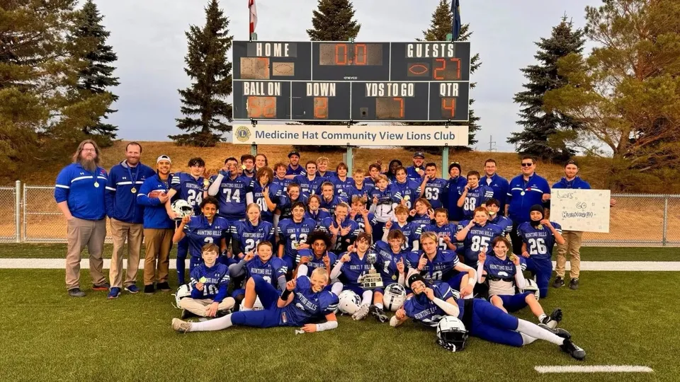 La squadra sportiva della Hunting Hills High School posa insieme davanti a un tabellone segnapunti all'aperto con pini sullo sfondo.