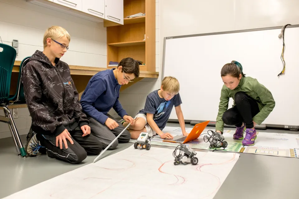 Quattro studenti della École du Bois-Joli lavorano sul pavimento dell'aula con piccoli robot e un computer portatile.