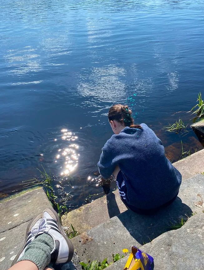 Studentessa seduta sui gradini in riva a un lago in una giornata di sole durante l'anno all'estero in Irlanda
