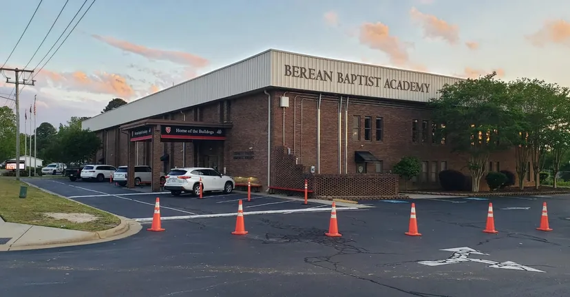 L'edificio in mattoni della Berean Baptist Academy è circondato da un parcheggio con veicoli e transenne.