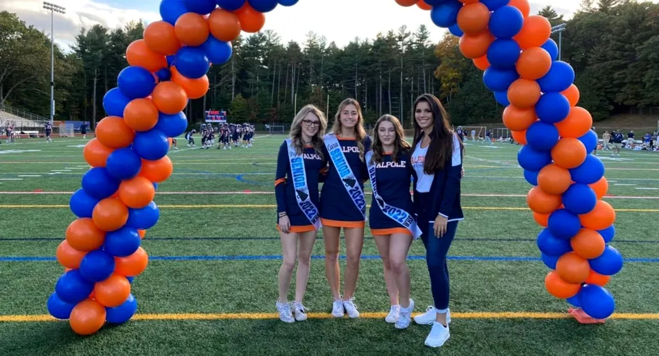 Quattro studentesse della Walpole High School sono insieme davanti a un arco di palloncini sul campo sportivo.